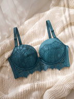 A teal blue lace underwire bra with scalloped edges and adjustable straps, styled flat on a cream-colored knit blanket.