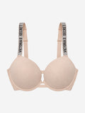 A light beige wireless bra with wide shoulder straps featuring the text 'VICTORIA'S SECRET' in black on a glittery background, shown against a plain light gray background.