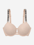 A light beige wireless bra with wide shoulder straps featuring the text 'VICTORIA'S SECRET' in black on a glittery background, shown against a plain light gray background.