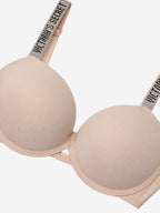 A close-up of a Victoria's Secret wireless bra in a light nude beige color, showing the smooth cup, underband, and the brand name printed on the shoulder strap.